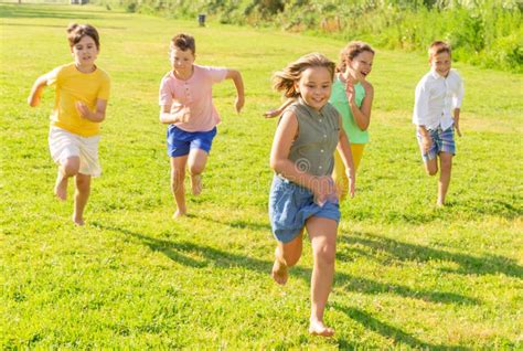Happy Preteen Friends Running Together On Green Meadow Stock Photo