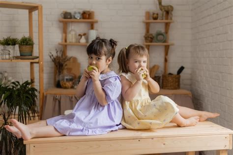 부엌에서 녹색 사과를 먹고 있는 드레스를 입은 두 명의 귀엽고 재미있는 소녀 텍스트 배너를 위한 공간 프리미엄 사진