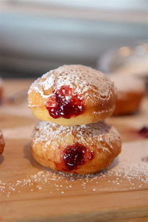 Jelly Donuts With Powdered Sugar Stacked On Top Of A Wooden Board