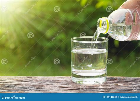 Female Hand Pouring Water From Bottle To Glass On Nature Background