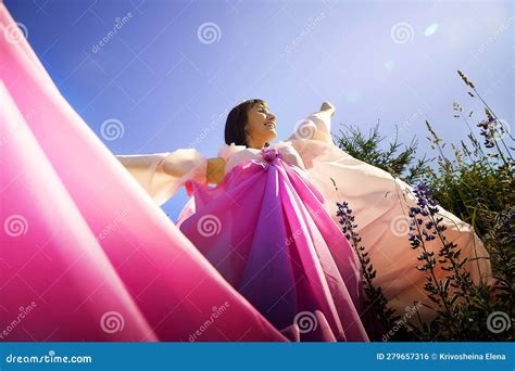 Beautiful Girl In A Lush Pink Ball Gown In Green Field During Blooming