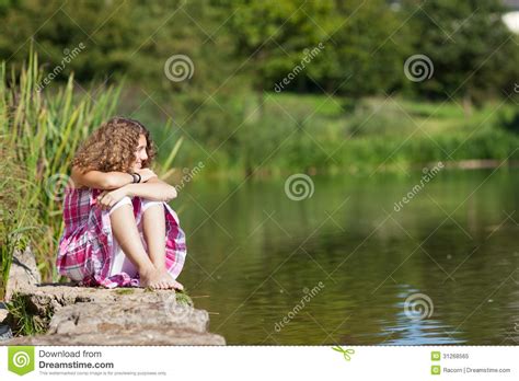 adolescente s asseyant sur la roche tout en regardant loin par le lac image stock image du