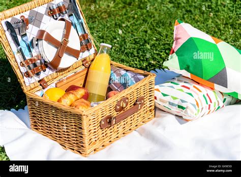 Picnic Basket Food On White Blanket With Pillows In Summer Stock Photo