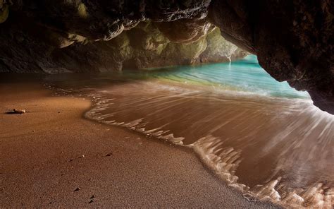 An Ocean Cave With Waves Coming In From The Water And Sand On The Beach