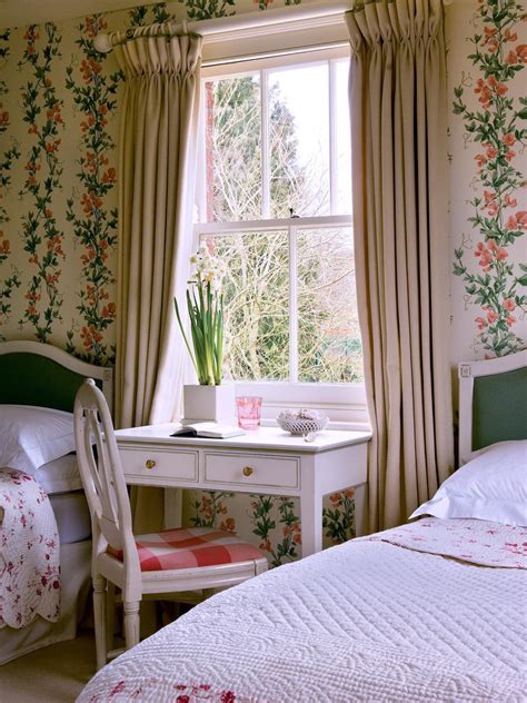 A shabby chic primary bedroom boasting a large bed setup with stylish bedside tables and a freestanding shelf. Refined Shabby Chic Bedroom With Floral Wallpaper | HGTV