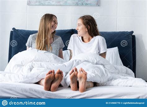Two Smiling Barefoot Lesbians Sitting On Bed And Looking At Each Other Stock Photo Image Of