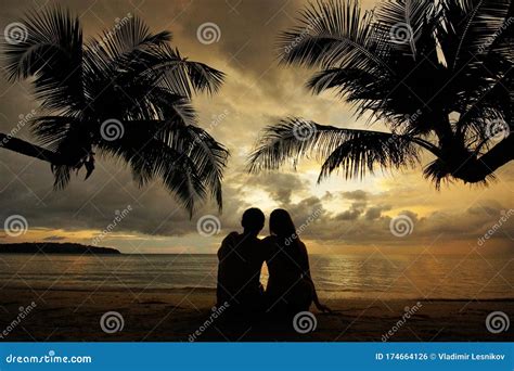 Silhouette Of Couple Sitting And Hugging On Tropical Beach At Sunset
