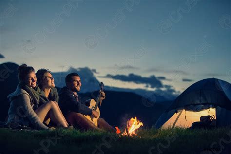 Three Friends Camping With Fire On Mountain At Sunset Stock Photo