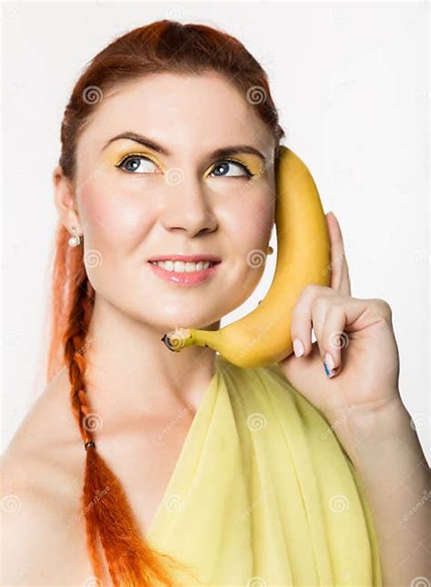 Young Redhead Woman Holding Banana Near Her Face Like Smartphone On A