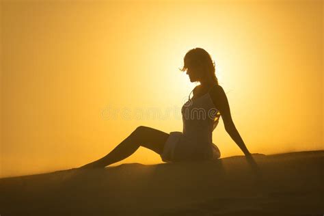 Silhouette Of Girl Sitting On The Sand Dunes In The Desert In The Sunset Light Stock Image