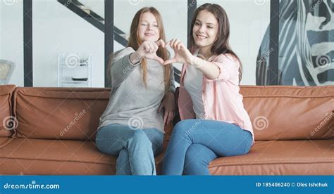 duas mulheres bonitas sorrindo sentadas no sofá e fazendo forma cardíaca com as mãos retrato de