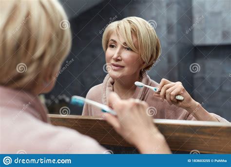 Teeth Health Mature Woman Uses Toothbrush In Front Of The Mirror