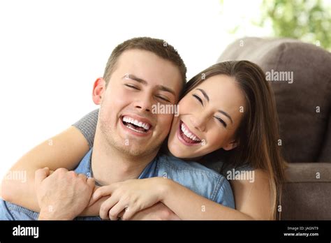 Happy Couple With Perfect White Smile Posing And Looking At Camera On A Couch At Home Stock