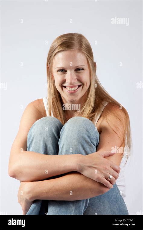 lovely blond woman sitting on a wooden stool with her knee raised up near her chin looking at