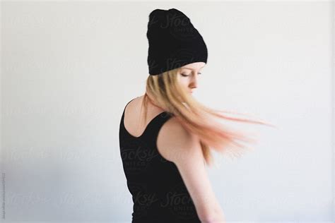movement shot of teen girl wearing a black beanie flicking her long blonde and pink hair by