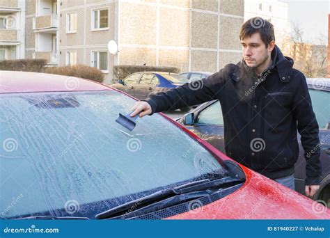 Man Is Scraping Ice From Frozen Windshield Window Of Car In Winter