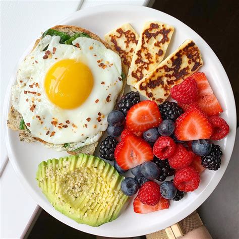 A White Plate Topped With Eggs Fruit And Toast Next To Sliced Avocado