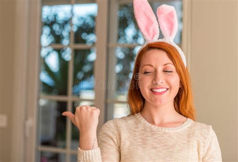 redhead woman wearing easter rabbit ears at home pointing with hand and finger up with happy