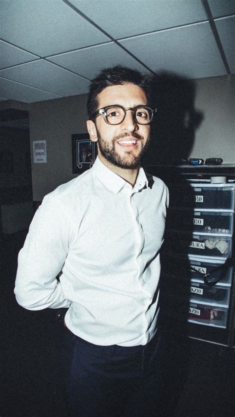 A Man Wearing Glasses Standing In Front Of A Filing Cabinet
