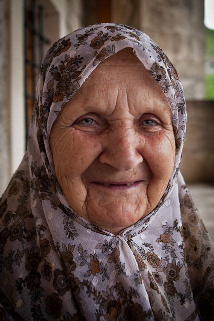 An Old Woman Wearing A Headscarf And Looking At The Camera With A Smile