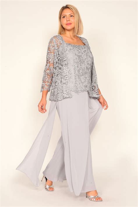a woman wearing grey pants and a top with lace overlays standing in front of a white background