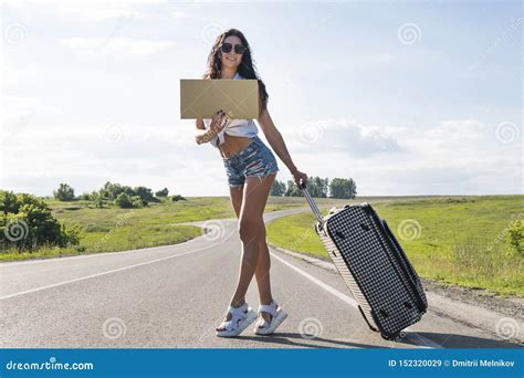 girl with tourist suitcase hitchhiking along a road and holding cardboard outdoor ready for