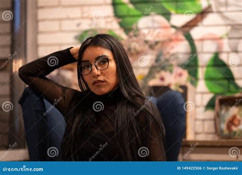 A Beautiful Girl Of Eastern Ethnicity Turkmen In Glasses Is Resting In A Cafe On The Couch