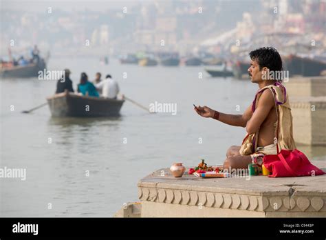 sadhu praying on the ghats lining the river ganges with a rowboat in the background varanasi