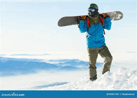 Snowboarder Standing At The Very Top Of A Mountain And Holding