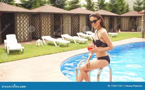 Glamour Girl In Trendy Swimsuit And Sunglasses Sitting By The Pool With Cocktail Stock Image