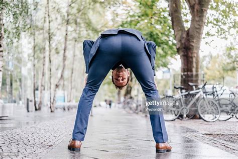Back View Of Businessman Bending Over On Pavement Looking Through His