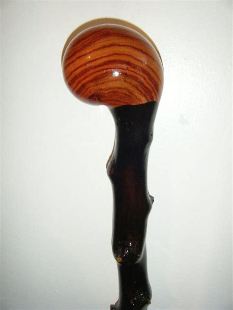 A Brown And Black Glass Object On A White Wall Next To A Wooden Stick