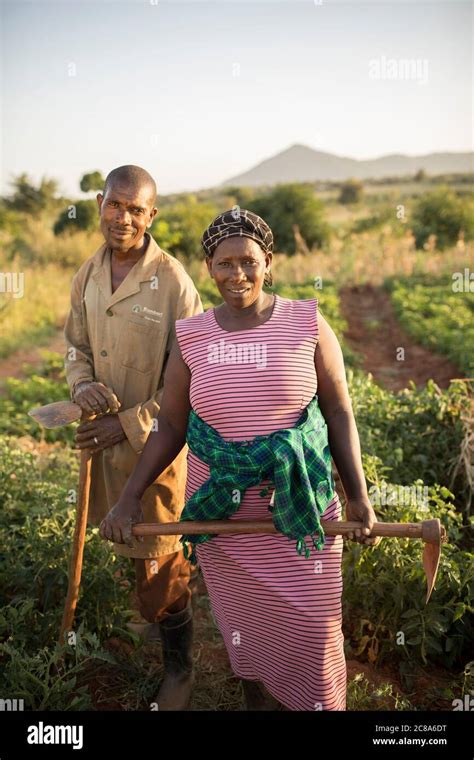 A Wife And Husband Stand Together Holding Hoes On Their Farm In Makueni