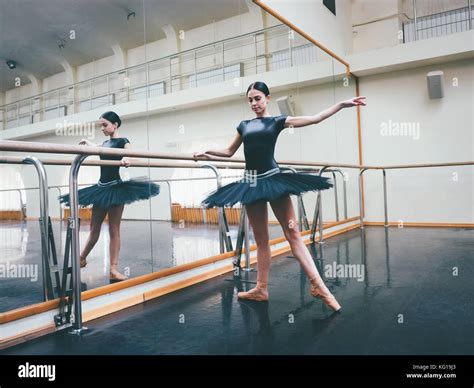 Ballerina In Black Tutu And Pointe Stretches On Barre In Ballet Gym