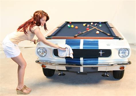 a woman leaning over a pool table in front of a white mustang with blue stripes