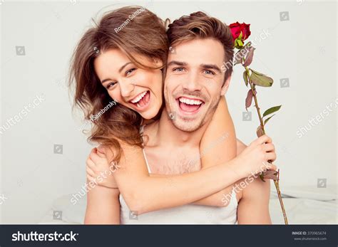 Cheerful Young Couple In Love Embracing In The Bedroom With Rose Stock