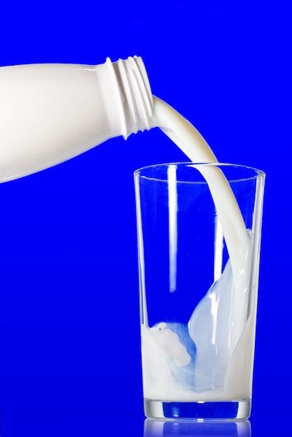 Premium Photo Milk Pouring From Bottle Into Glass On Blue
