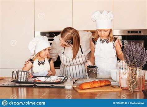 Young Mother Helps Her Two Daughters Cook Dough In The Kitchen Stock