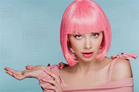 Beautiful Shocked Girl In Pink Wig Posing With Shrug Gesture Isolated On Blue Stock Photo