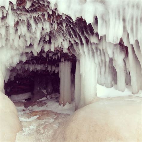 An Ice Cave With Icicles Hanging From Its Ceiling And Snow On The Ground