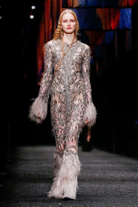 A Woman Walking Down A Runway In A Dress With Feathers