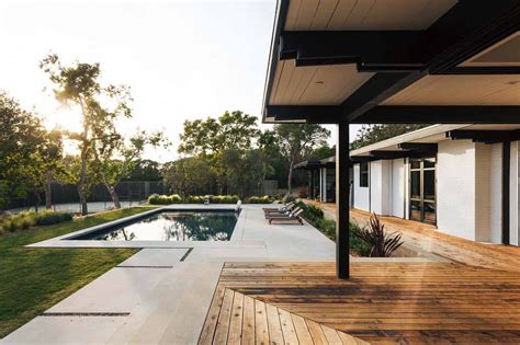 An Outdoor Swimming Pool Surrounded By Wooden Decking And White Walls With Trees In The Background