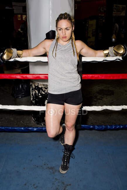 portrait of female boxer leaning against boxing ring ropes full length — boxing glove only