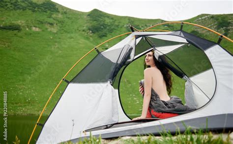 Back View Of Beautiful Naked Woman Traveller Sitting In Tent In Sleeping Bag Enjoying Beautiful