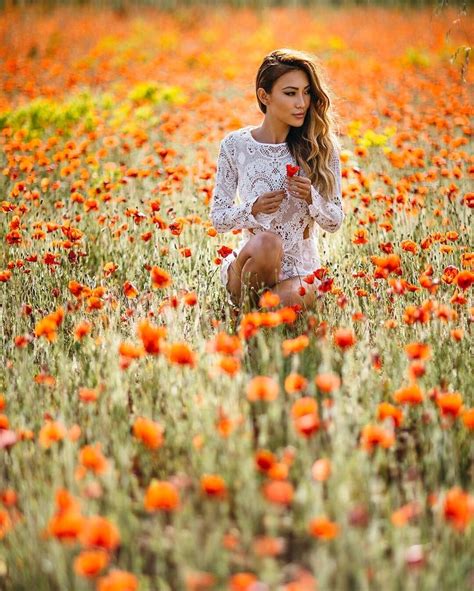 A Woman Kneeling In A Field Of Flowers Holding A Red Flower And Looking