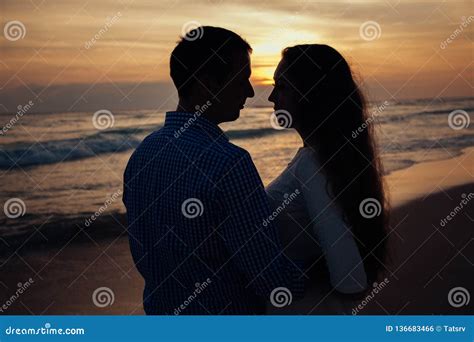 Two Young Lovers Standing On A Beach And Looking To Each Other On