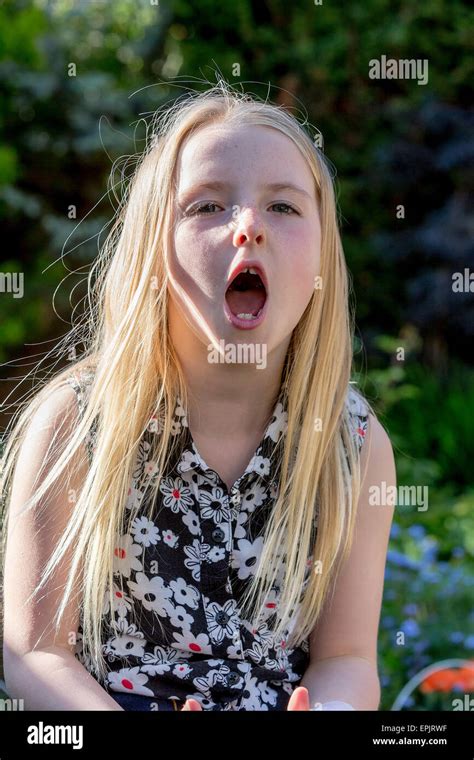 Blonde 8 Year Old Girl Sitting In A Garden Shouting At The Photographer