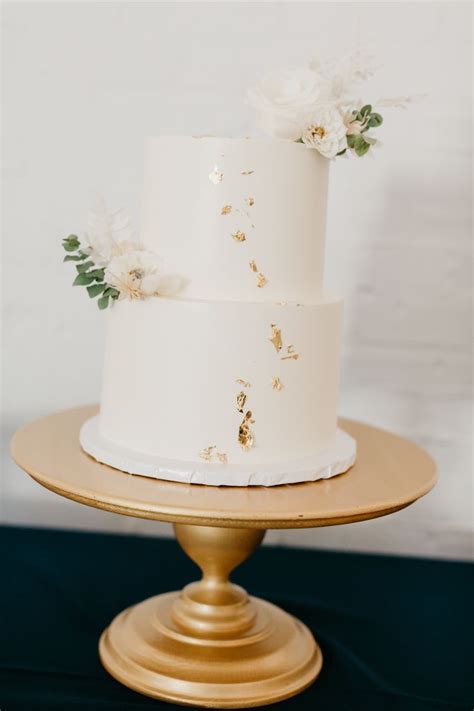A Three Tiered Cake With White Flowers On Top Is Sitting On A Gold Plate