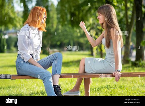 Two Young Women Friends Sitting On A Bench In Summer Park And Talking