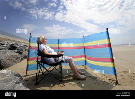 A Old Age Pensioner Enjoys Sunbathing On A British Beach With Stock